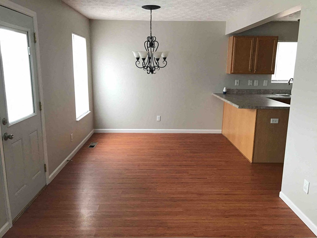 an empty living room with wood floors and a kitchen