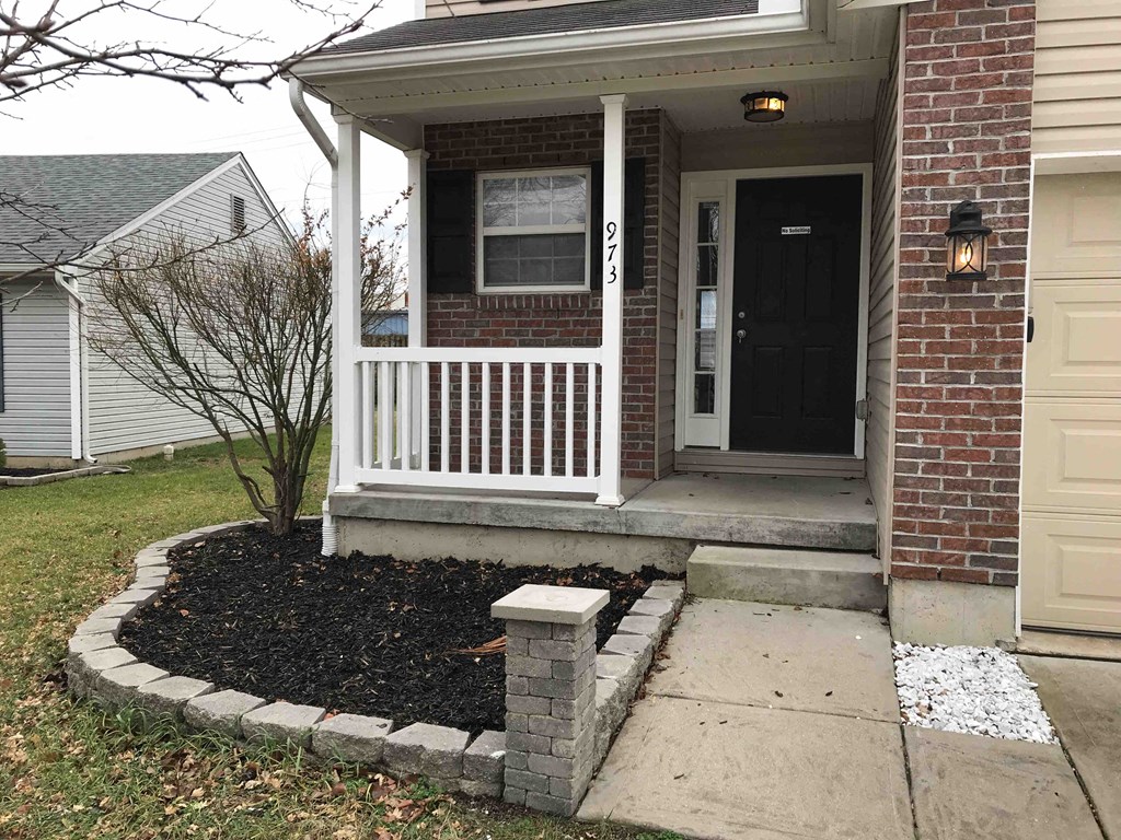 front porch of a brick house with a white railing and a walkway leading up