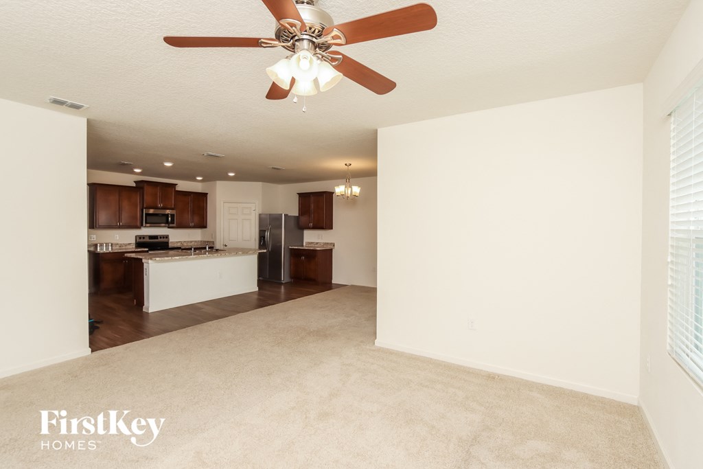 an empty living room with a ceiling fan and a kitchen