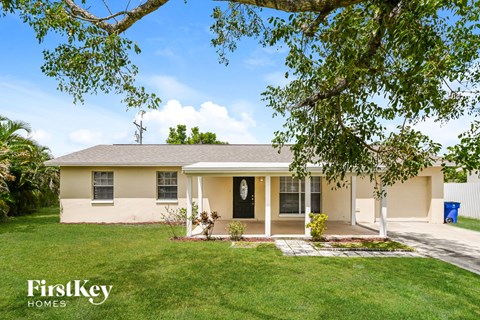 A house with a white front porch and a tree branch in the foreground.