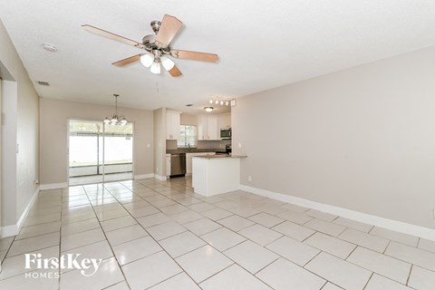 A spacious room with a fan and a kitchen in the background.