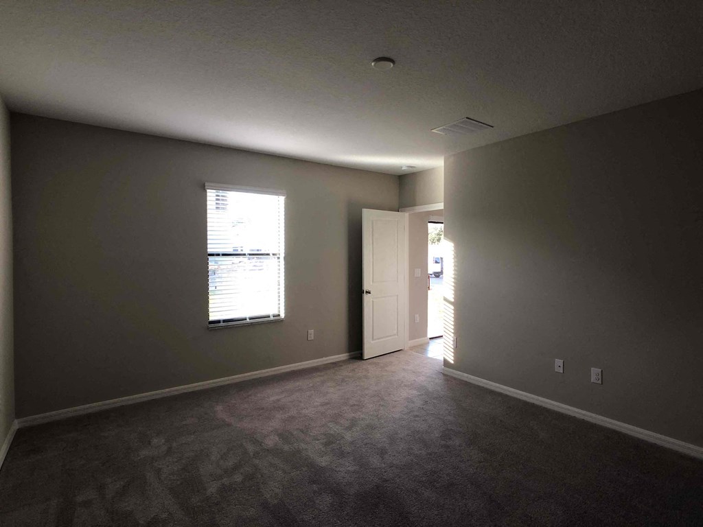 A room with a carpeted floor and a window with blinds.