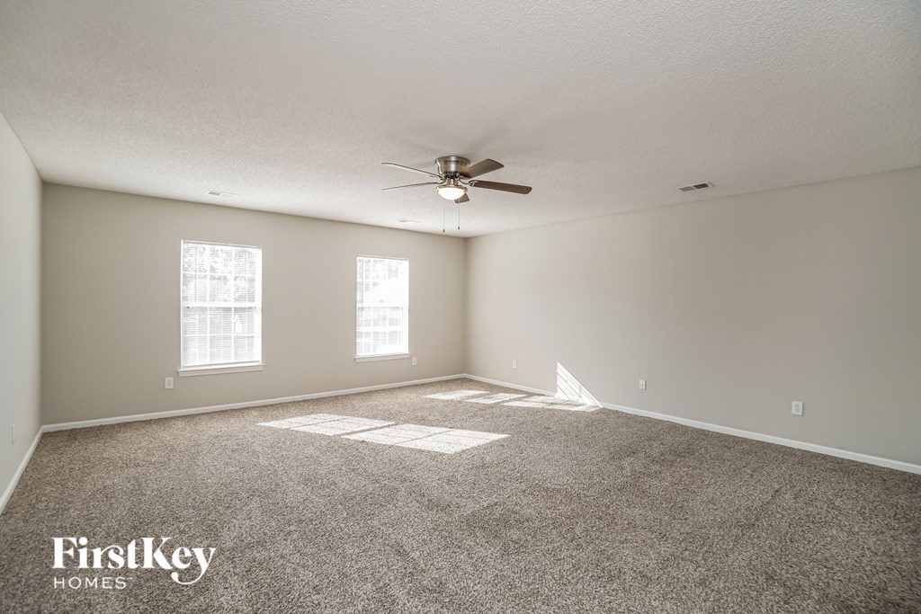 A spacious room with a carpeted floor, a ceiling fan, and two windows.