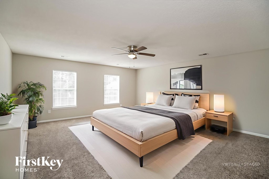 A bedroom with a large bed, a ceiling fan, and a potted plant.