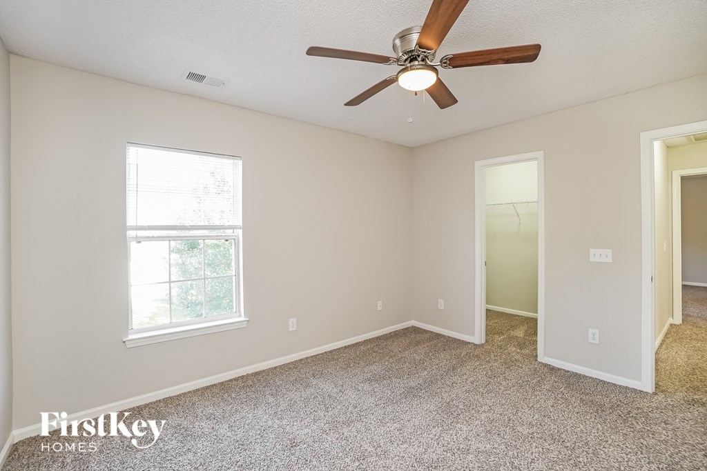A room with a carpet floor, a ceiling fan, and a window.