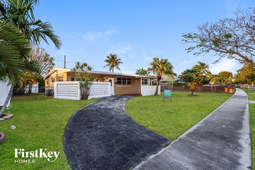 a house with a driveway and a yard with grass and palm trees