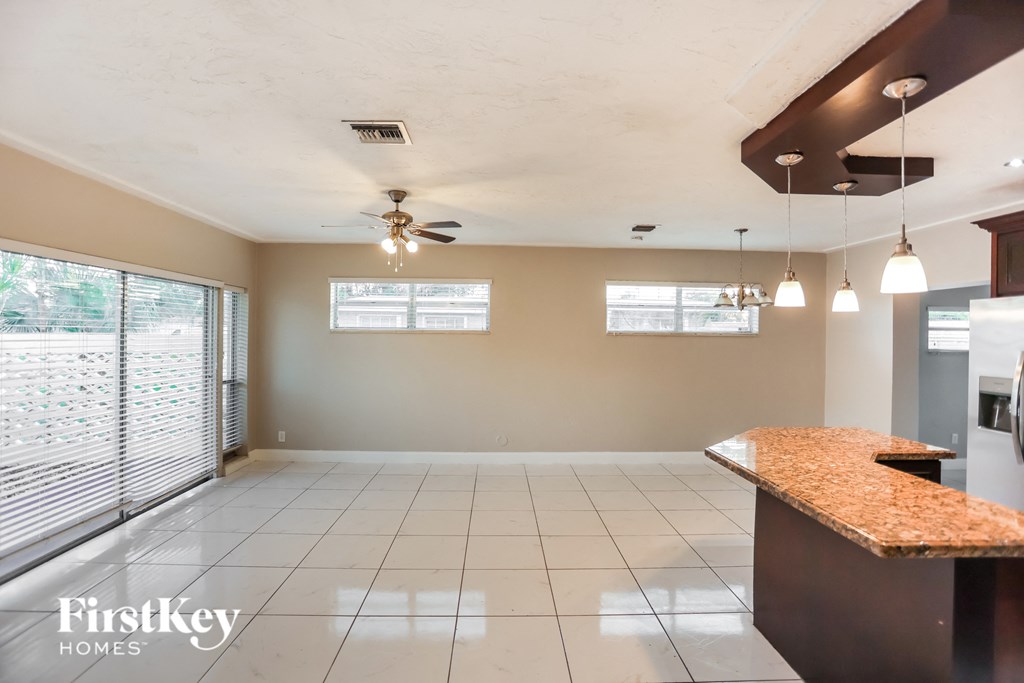 an empty living room with a kitchen and a ceiling fan