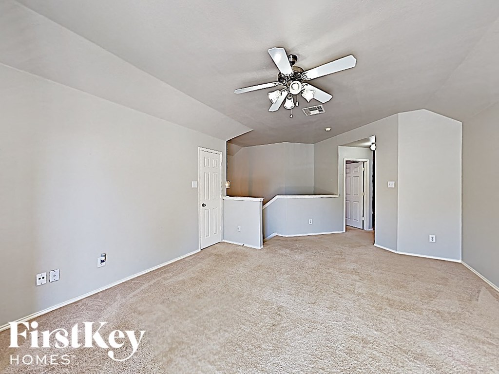 an empty living room with a ceiling fan and a kitchen