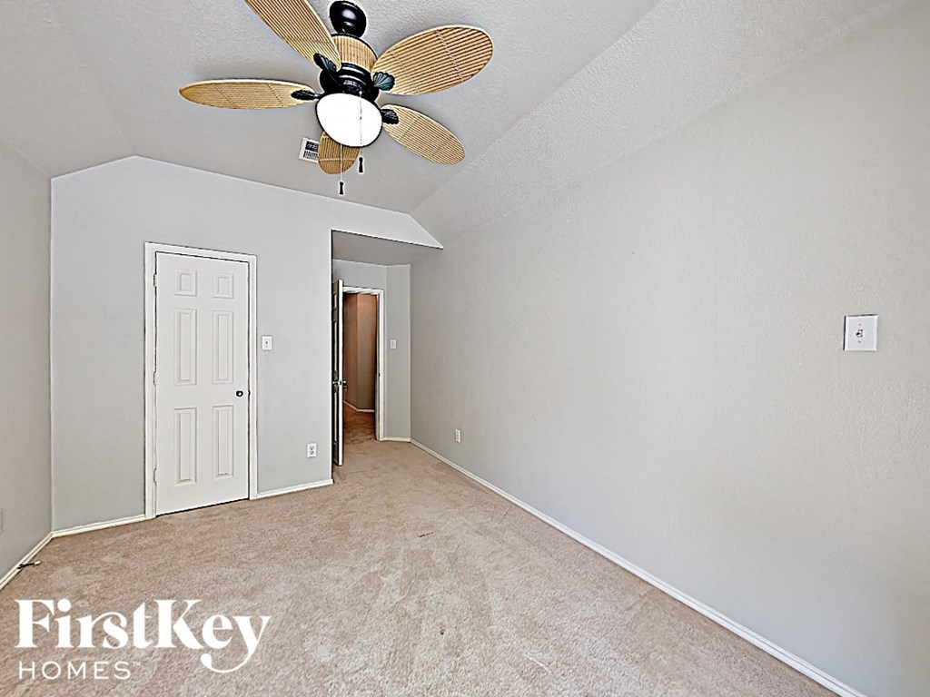 an empty bedroom with a ceiling fan and a door to a hallway