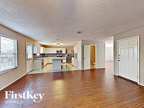 A spacious living room with wooden floors and a kitchen in the background.