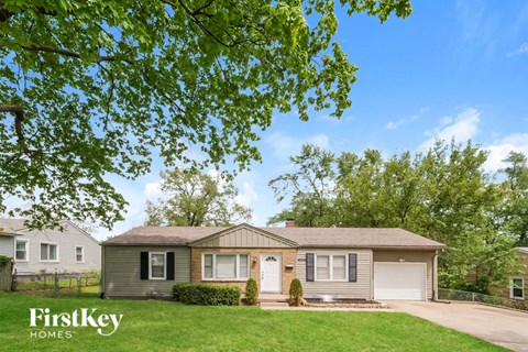 A house with a brown roof and a white garage door is surrounded by greenery.