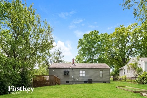 A house with a brown roof and a porch is surrounded by green trees.