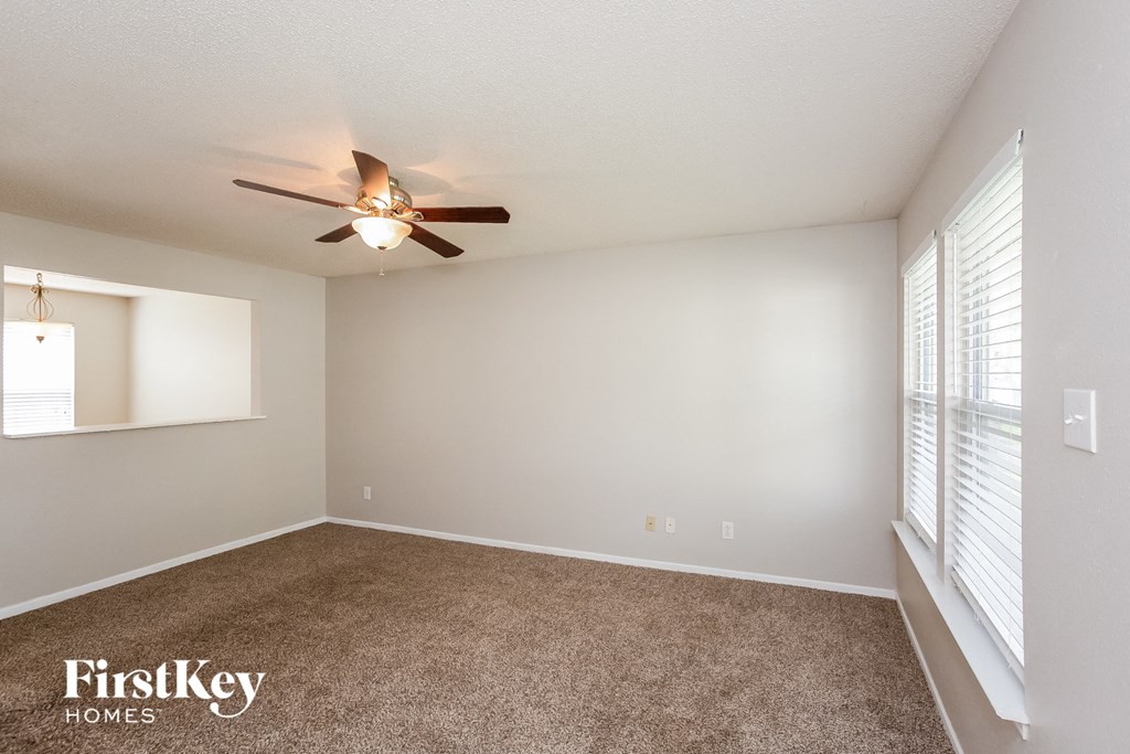 the spacious living room with large windows and a ceiling fan
