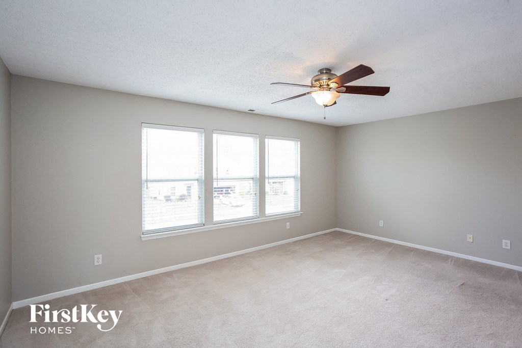 an empty living room with a ceiling fan and three windows