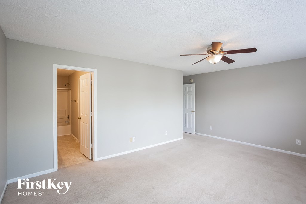 an empty living room with a ceiling fan and a door to a hallway