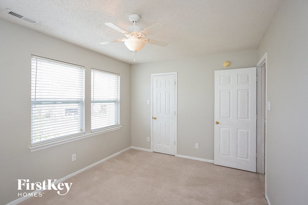 a bedroom with a ceiling fan and two windows