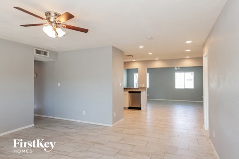 A spacious room with a ceiling fan and a kitchenette in the background.