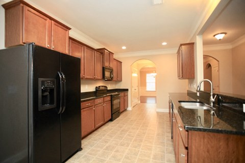 A black refrigerator is in the corner of a kitchen with wooden cabinets.