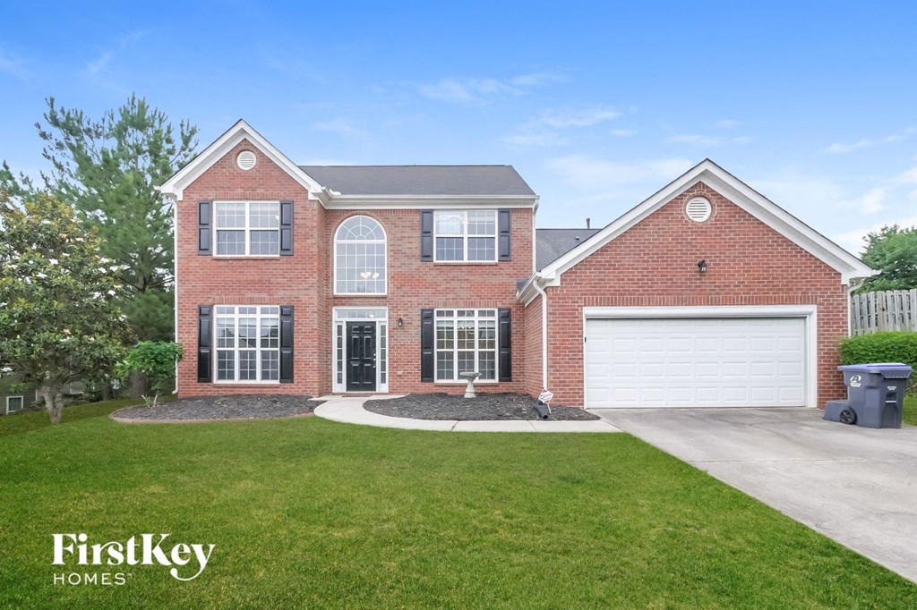 A brick house with a garage and a tree in front.