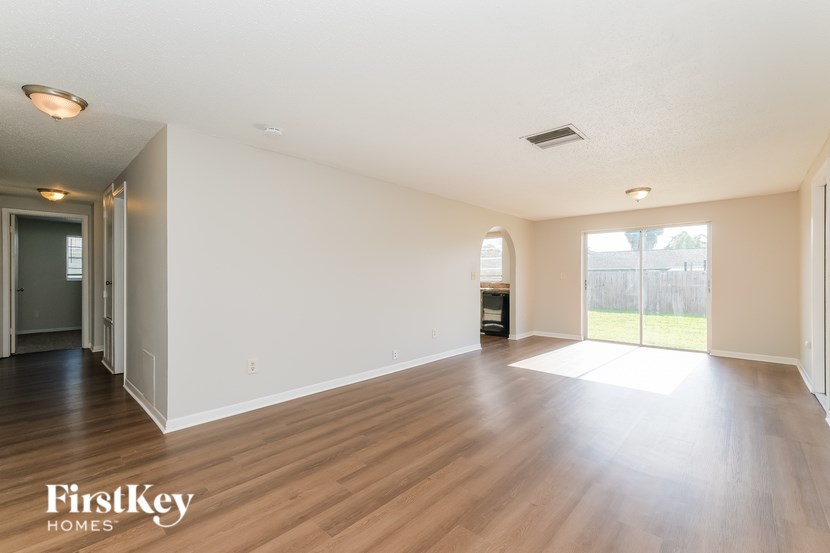 A spacious empty room with wooden flooring and white walls.