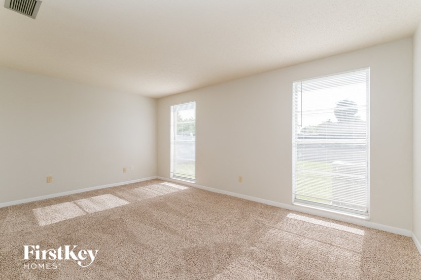 A room with a carpet floor and a window showing a view of a house.