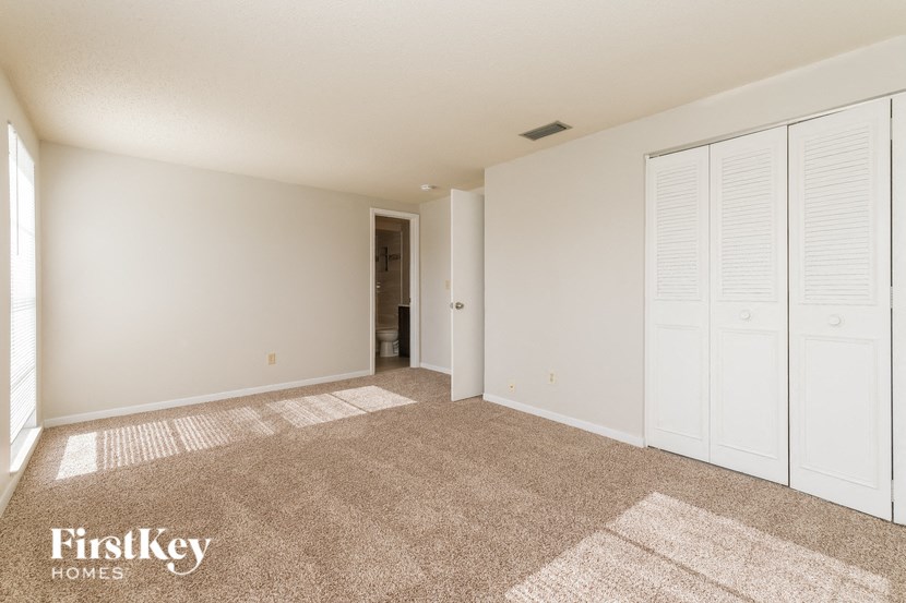 A room with a carpeted floor and white walls, with a doorway leading to another room.