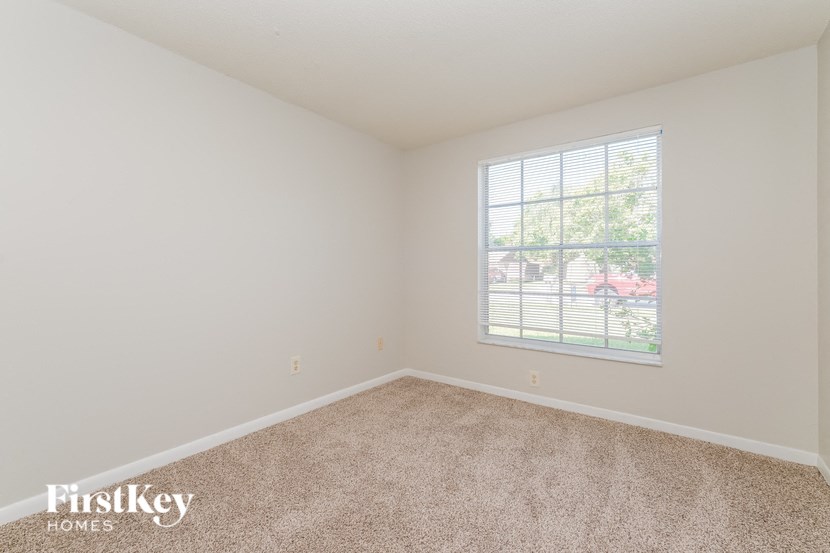 A room with a carpeted floor and a window showing a view of a residential area.