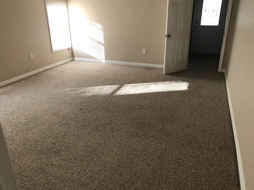 A room with carpeted floor and a door on the right side.
