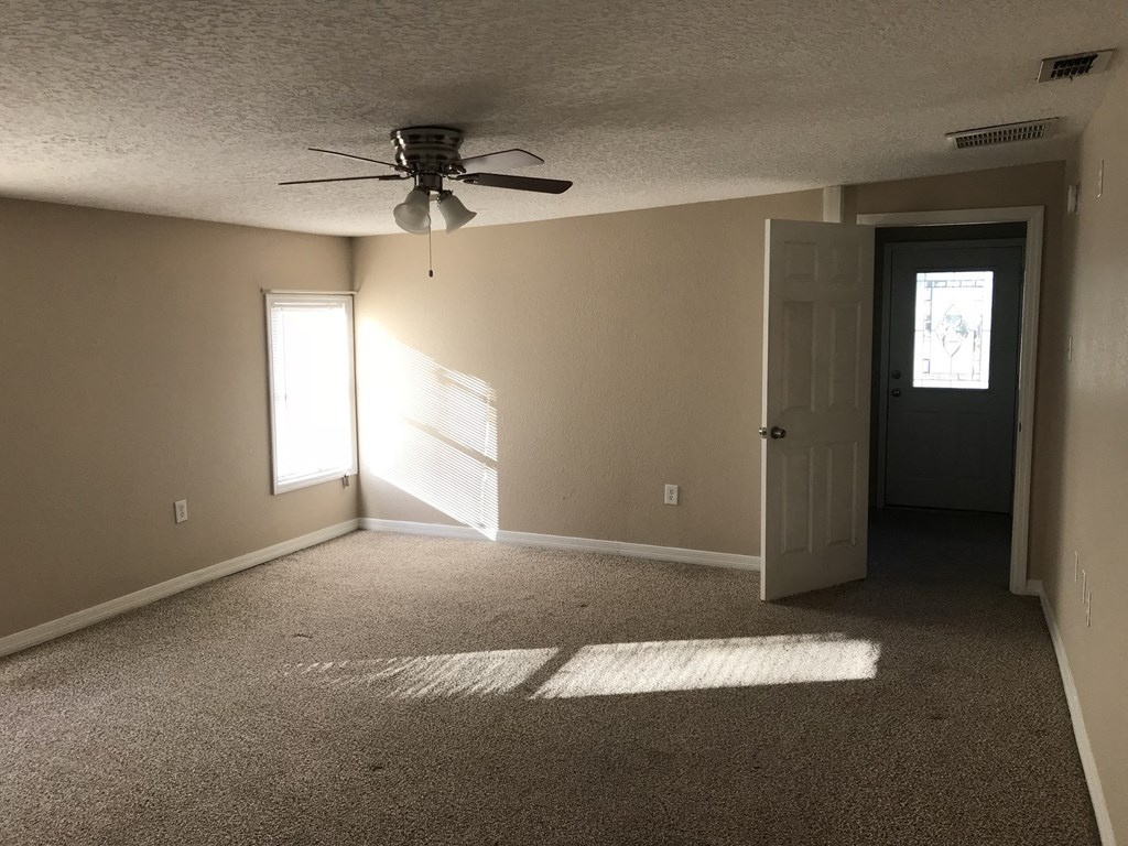 A room with a ceiling fan and a door leading to another room.