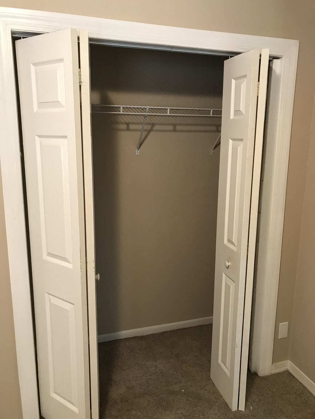 A white closet with a door open and clothes hangers inside.