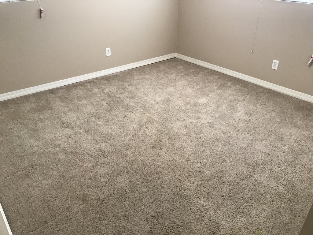 A room with a carpeted floor and two electrical outlets on the wall.