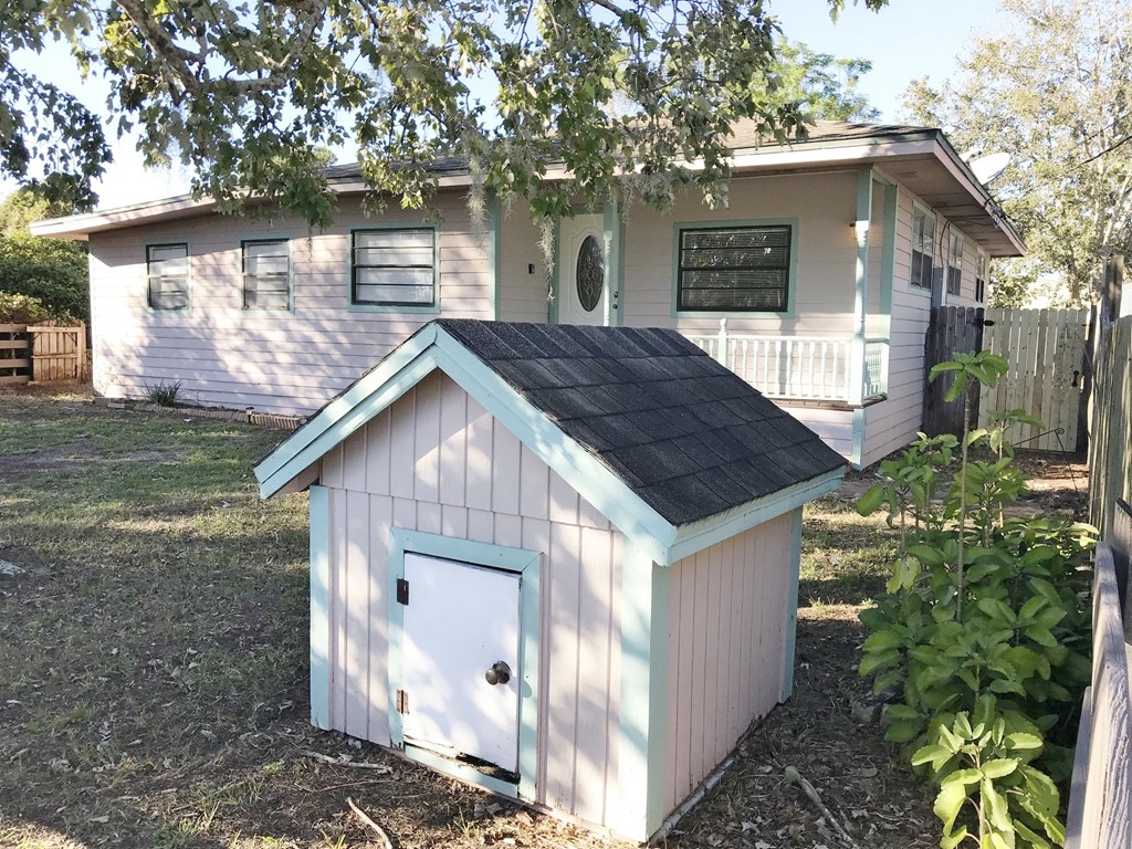 A small house with a white door and a black roof is in front of a larger house.