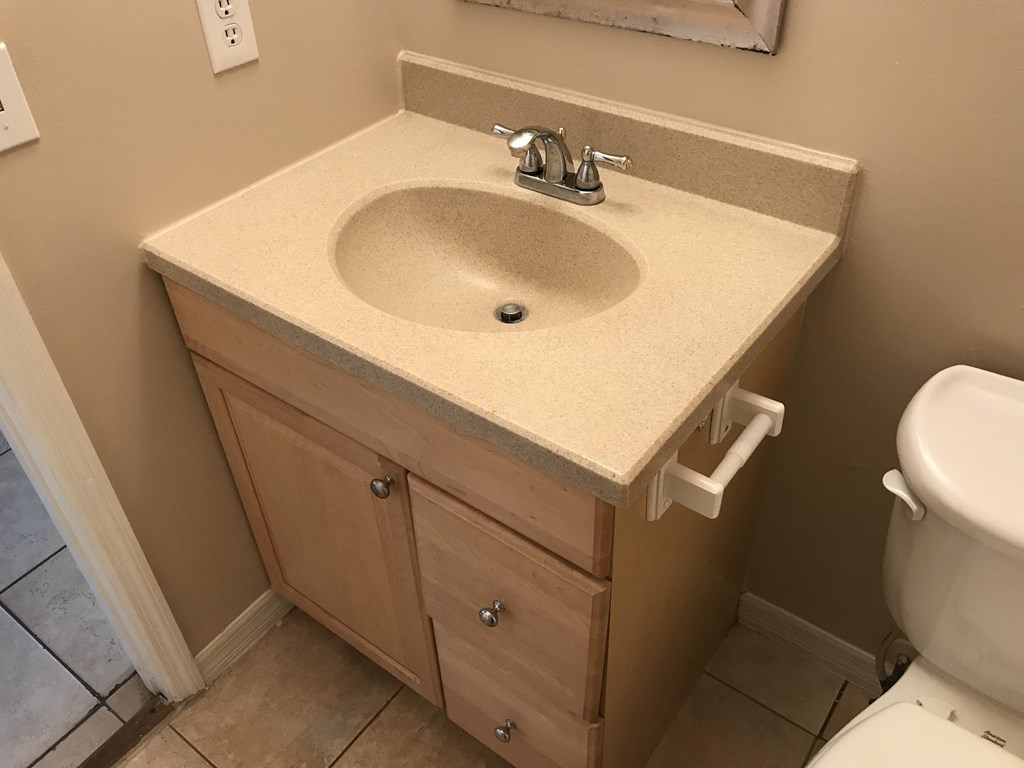 A bathroom sink with a wooden cabinet and a toilet in the background.