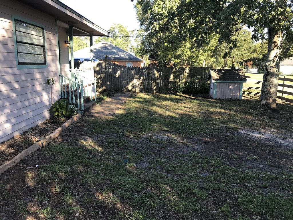 A backyard with a pink house, a tree, and a shed.