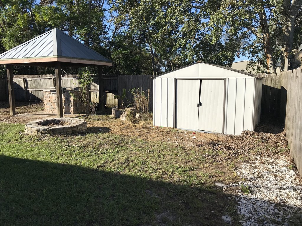 A white shed sits in a yard next to a wooden fence.