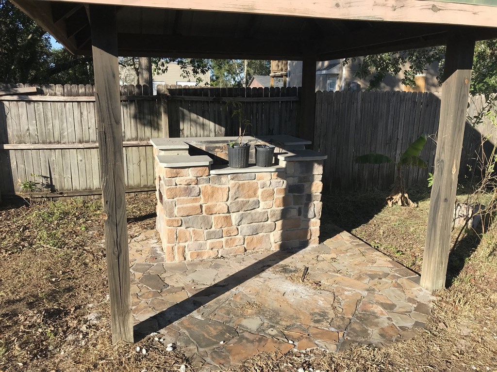 A brick oven is under a wooden pergola in a backyard.