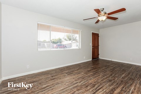 an empty living room with a large window and a ceiling fan