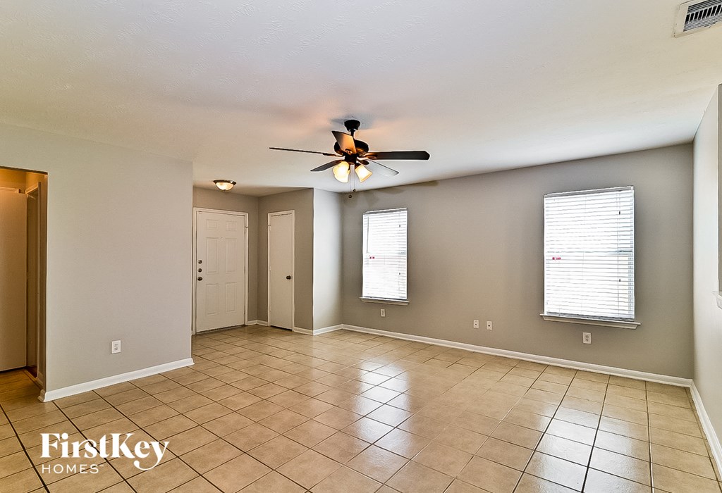 an empty living room with a ceiling fan and tiled floors