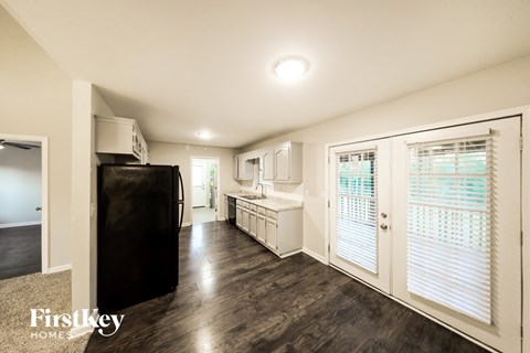 A black refrigerator in a kitchen with wooden floors and white walls.