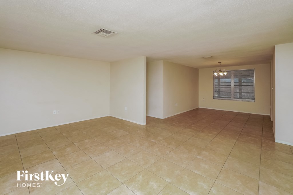 A room with beige tiled flooring and white walls, with a window covered by blinds.