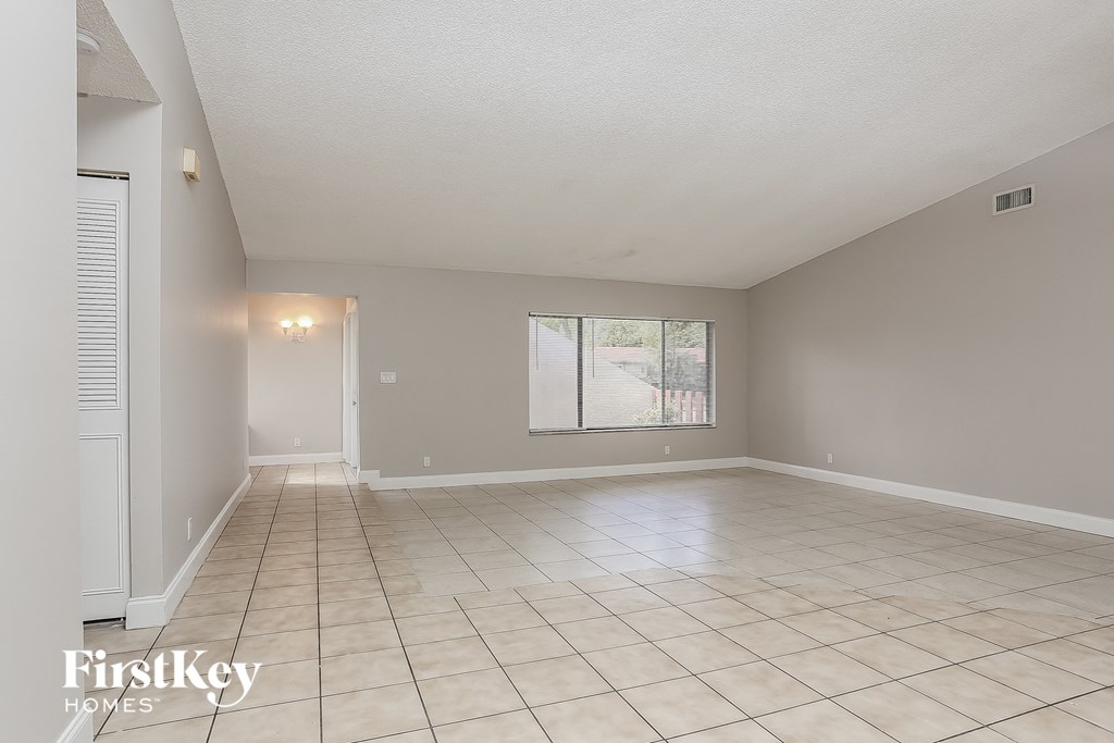 A spacious empty room with tiled flooring and a window.