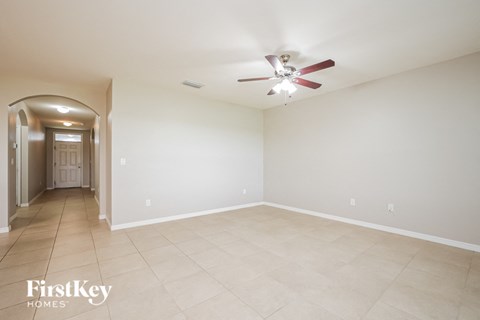 A spacious room with a fan and a doorway leading to another room.