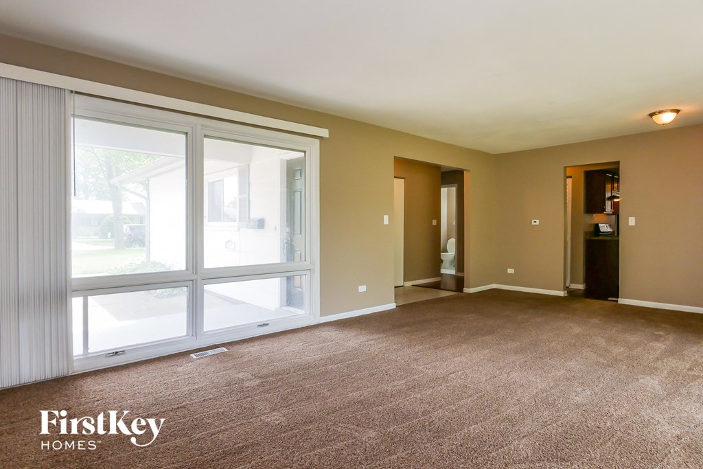 A spacious room with a carpeted floor and a large window with sliding doors.