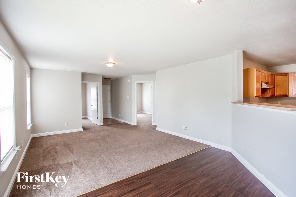 a living room with white walls and wood flooring and a kitchen