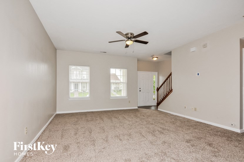 an empty living room with a ceiling fan and a staircase