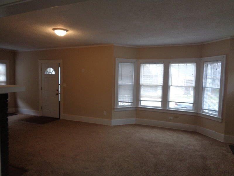 an empty living room with three windows and a door