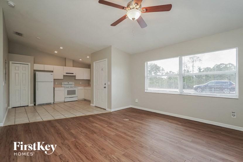 A spacious empty room with a ceiling fan and wooden flooring.