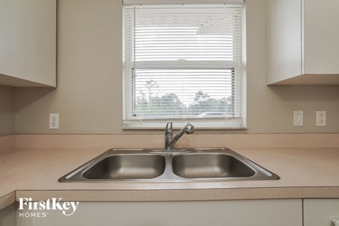 A kitchen with a double sink and a window with blinds.