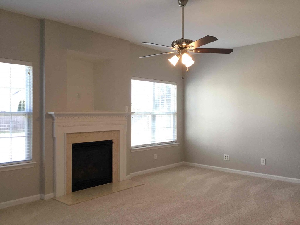 A room with a fireplace, a ceiling fan, and two windows.