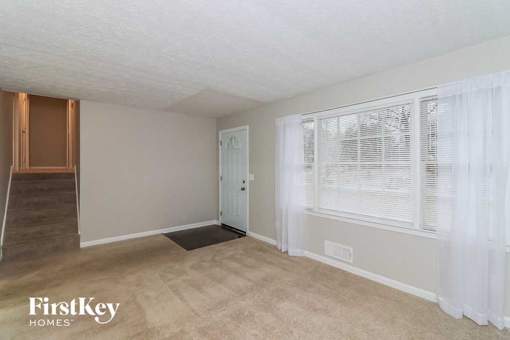 A room with a carpeted floor and a window with white curtains.